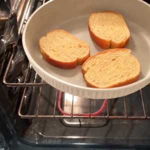 cream-frying-pan-in-oven Cream ribbed frying pan without its handle, holding three bread slices inside an oven.